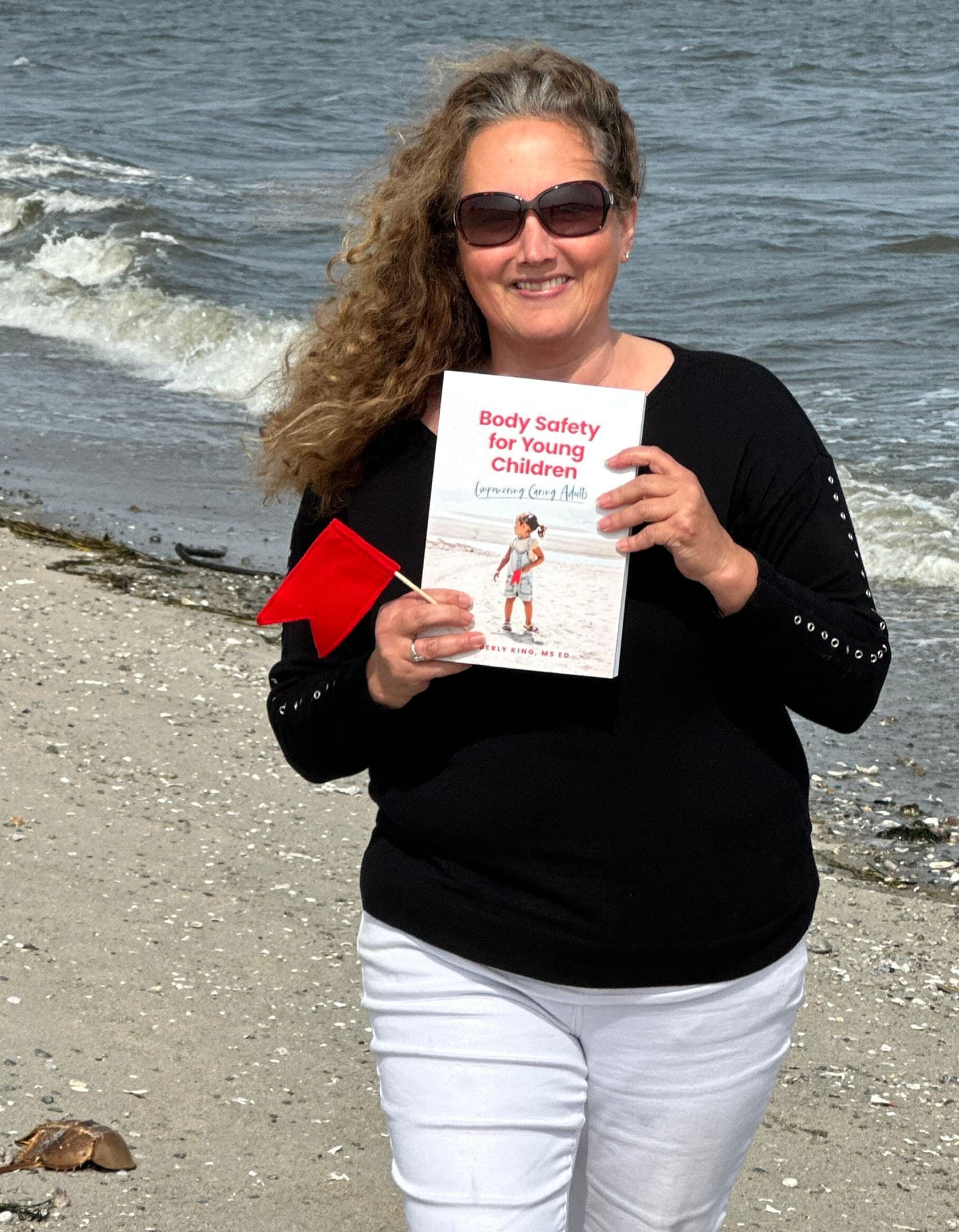 Kimberly King holding her book Body Safety for Young Children on the beach